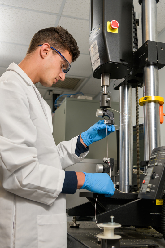 CCM researcher in white lab coat and safety googles using lab instument.