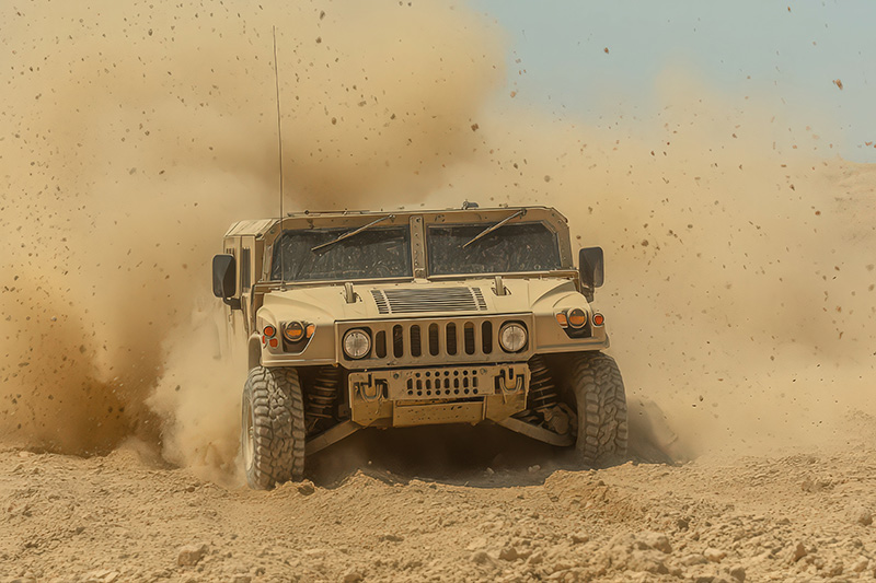 Humvee driving through sand throwing up a large cloud behind it.