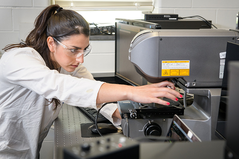 Student intern in white lab coat adjusts a piece of equipment in the lab.