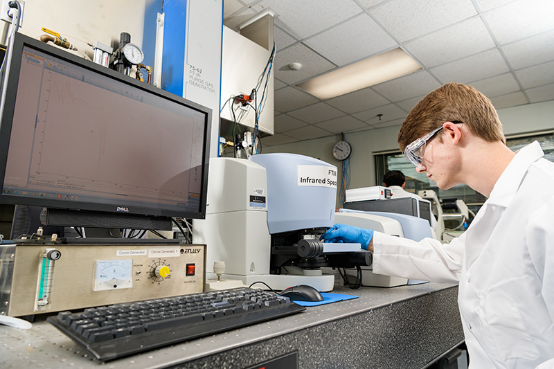 Student intern in while lab coat and safety goggles adjusts an imaging device in the lab.
