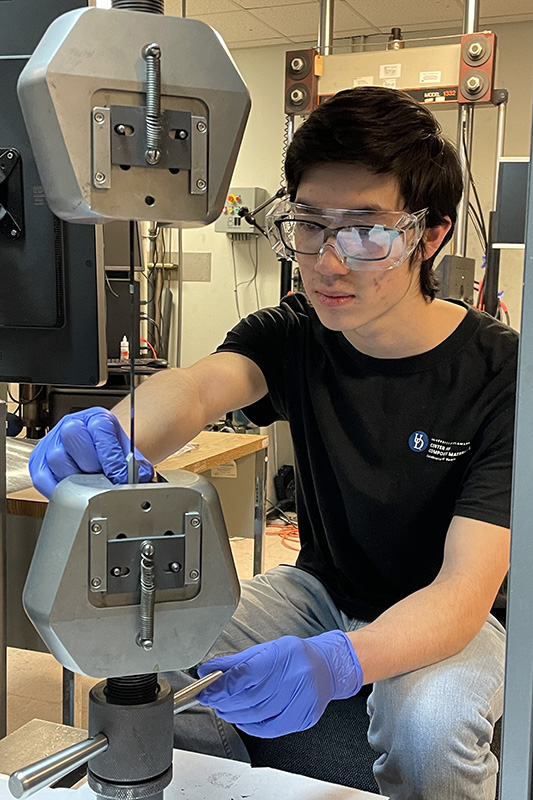 Summer intern in black t-shirt and safety goggles set up a tension test on lab equipment.