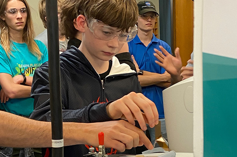 A young student is guided to activating some equipment.