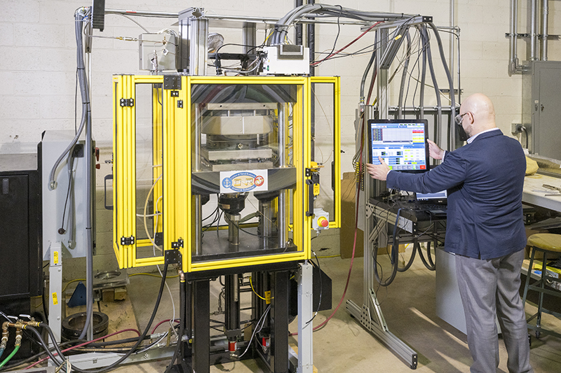 Summer intern in black t-shirt and safety goggles set up a tension test on lab equipment.
